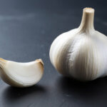 Один очищенный зубчик чеснока и головка чеснока крупным планом