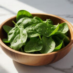 Свежие листья шпината в тарелке, содержание пуринов в зелени и влияние на мочевую кислоту.
