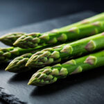 Свежие стебли зеленой спаржи на темной поверхности — анализ содержания пуринов для рациона ЗОЖ.