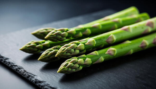 Свежие стебли зеленой спаржи на темной поверхности — анализ содержания пуринов для рациона ЗОЖ.