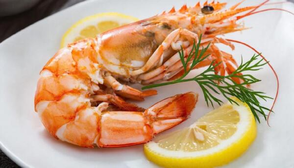 Одна вареная королевская креветка на белой тарелке с лимоном