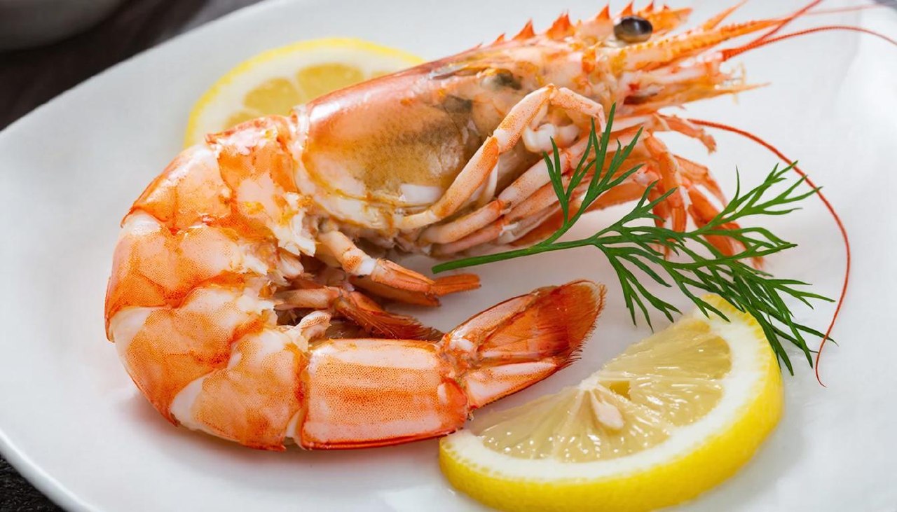 Одна вареная королевская креветка на белой тарелке с лимоном