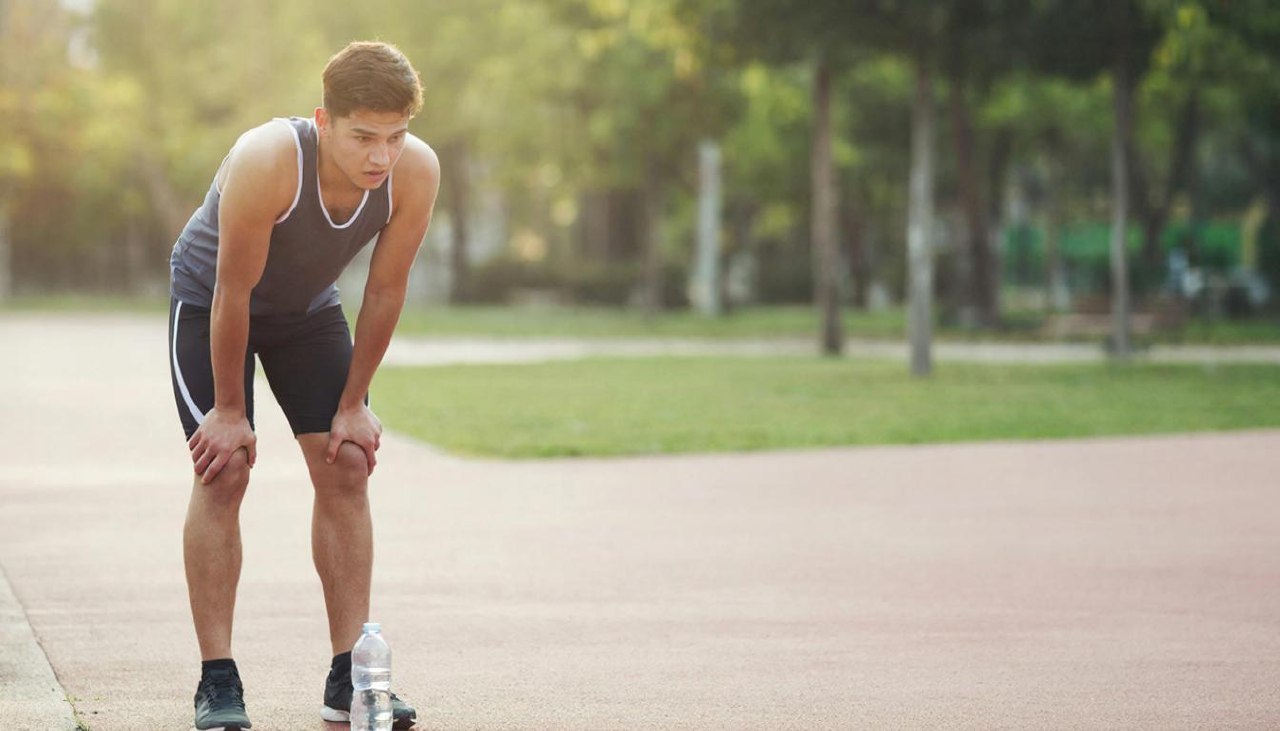 Мужчина атлет восстанавливает дыхание после пробежки в парке